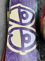 Close-up of skateboard deck with stylized eyes graphic on purple wood.