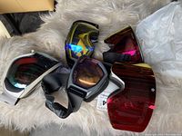 Five snowboard goggles laid out on fur surface showing various lens colors including red, yellow, blue and mirrored finishes.