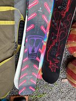 Four snowboards stacked on the ground, showing topsheet graphics and edge wear.
