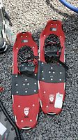 Pair of red Little Bear Trek snowshoes size 30 side by side on gravel ground, showing full snowshoe shape and bindings.
