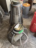 Two wicker style metal solar lanterns on concrete floor, one larger tapered shape and one smaller round shape.