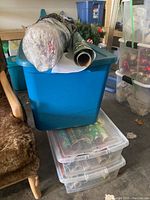 Blue storage tub with bubble wrapped rolls of wrapping paper on top and sheets of holiday wrapping paper inside clear plastic tubs below.