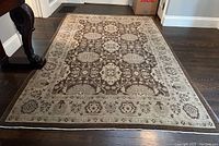 Full view of rectangular 6x9 area rug on hardwood floor showing brown background with beige medallion and floral motifs