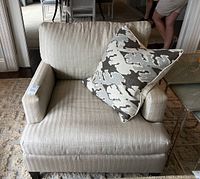 Front view of beige linen T-back armchair with down cushions and decorative pillow.