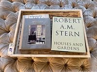 Three coffee table books on architecture and interior design displayed together on a wooden inlaid tray placed on a tufted upholstery surface.