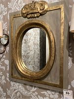 Full front view of square wood frame with oval mirror inset and decorative crest