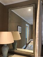 Full-frontal view of rectangular mirror leaning against wall with lamp in foreground