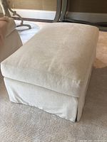 Front three-quarter view of ottoman on carpet with adjacent sofa.