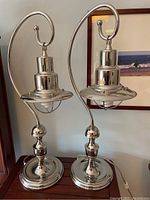 Pair of lamps side by side on wood surface with framed artwork behind