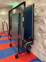 Side view of folded table showing blue panels, black metal frame, caster wheels, Butterfly and Playback Rollaway branding
