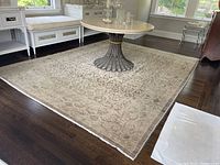 Full view of beige taupe area rug under round pedestal table and bench seating