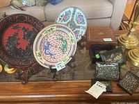 Full view of three plates on wooden stands, wooden box, and set of nesting boxes on glass-top table