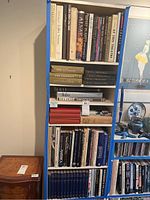 Books on six shelves in tall blue bookshelf including art and history titles, showing spines and dust jackets.