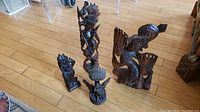 Set of four carved wooden figurines displayed on a wooden floor, varying sizes and styles