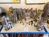 Photo showing collection of Gault miniature houses arranged in rows with some trees and miniature people in front and street decorations.