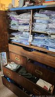 Wooden shelving cabinet with multiple plastic-wrapped dress shirts on shelves and three drawers below
