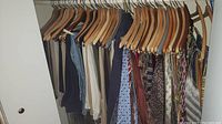 Closet rail with men's pants in neutral colors hung on wooden hangers.