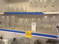 Multiple stemware pieces on two cabinet shelves, top shelf tall flutes, bottom shelf cut-crystal goblets.