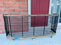 Front view of the antique fire fender showing curved brass top rail, black wire mesh, and brass base with feet.