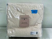 Quilt folded inside clear plastic packaging, label showing brand Bombay and product name Ivory Satin Quilt.