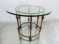 Front angled view of the side table showing the clear round glass top and brass colored metal frame with vertical supports and circular base.