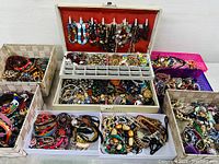 Overview of assortment of costume jewelry pieces in multiple trays and baskets, showing bracelets, necklaces, earrings, and brooches mixed together