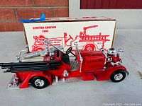 Front angle view of the red 1937 Ahrens-Fox fire truck model showing detailed features and open box with 1993 limited edition print.