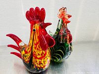 Front view of two blown glass rooster sculptures highlighting colors and shapes