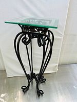 Full view of the side table showing its wrought iron base and glass top from an angled side perspective