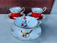Two Royal Albert Regal Series Red tea cups and matching saucers in red with gold trim in front of brick wall.