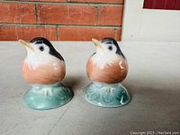 Pair of fat baby robin porcelain figurines from front angle showing peach breast, black head, white neck, and greenish base.