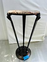 Front view of the tall round plant stand showing marble top and carved lion head detail on one leg