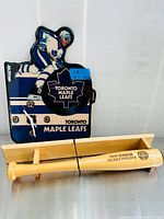 Wide shot showing the full Toronto Maple Leafs hockey player wall clock with clock hands and numbers, alongside the 2014 Blue Jays wooden decorative baseball bat on a stand.