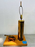 Full view of the lamp showing brass artillery shell casing mounted on a wooden base next to a miniature brass cannon on wooden carriage.