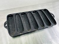 Top front angle view of vintage black cast iron cornbread pan with corn cob molds showing detailed kernel texture on six molds and one handle visible