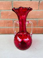 Front view of cranberry glass vase showing ruffled top, two clear glass handles, and quilted diamond pattern on the bulbous base.