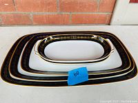 Four Edelstein porcelain trays stacked showing cobalt blue border with gold geometric and line detail and two trays with handles