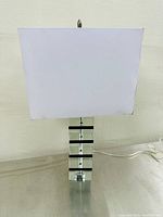 Full view of vintage Mid-Century Modern style stacked lucite table lamp with square white fabric shade on a metallic surface.