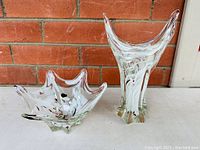 Both clear sculptural art glass pieces displayed side by side showing overall shape and coloration.