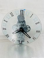 Front view of vintage skeleton quartz mantel clock with clear glass dial, black Roman numerals, black hands, and visible silver gears.