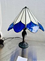 Front and side view of the stained glass table lamp showing Tiffany style blue and white petals on the shade and metal base.