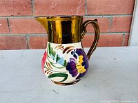 Front angled view of the Wade copper luster floral pitcher showing the spout, handle, and floral decoration on the body.