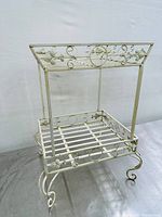 Full view of white wrought iron plant stand showing two-tier shelves and decorative scrollwork.