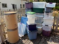 View of 25 various plastic storage bins and two large round fiberboard storage/mailing tins with metal rims and lids.