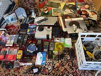 Overview of the electronics lot including NES console, remote controls, calculators, cameras, LPs and other accessories spread on a patterned rug.