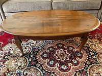 Front view of oval wooden Ethan Allen coffee table on patterned rug, showing wood grain and minor surface wear.