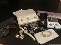 Full lot shot showing sunglasses, pins, watches, pearl necklace, crosses, and jewelry in boxes