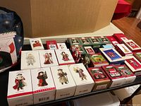 Wide view showing multiple Hallmark Keepsake ornament boxes and some plastic tote bag, sorted on table