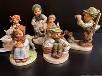 Five Hummel porcelain figurines with animals arranged together on black background.