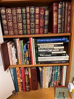 Three wooden shelves showing top row of leather bound classics and middle and bottom shelves of assorted books